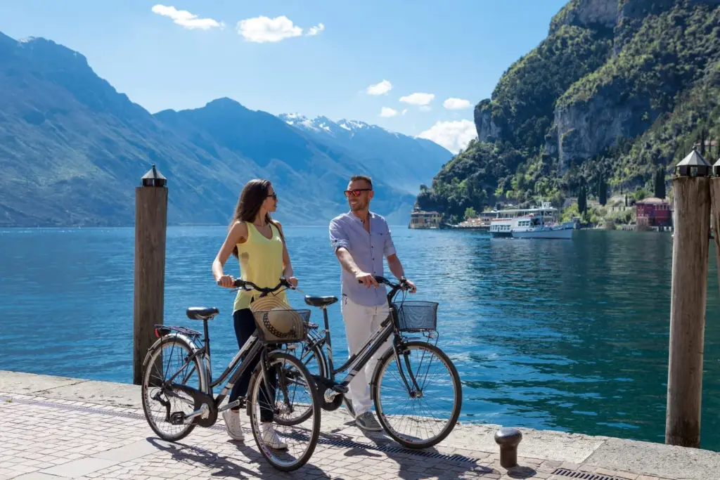 Coppia in bici lungo lago con paesaggio montano.
